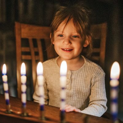 Adee Briggs, 3, learns about Chanukah and lights the Menorah candles for the first time. Photo by Sue Rollyson